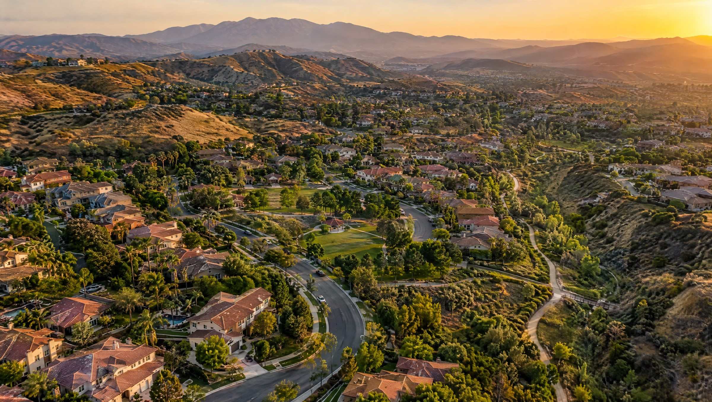 Aerial view of a Santa Clarita Valley neighborhood with tree-lined streets, green lawns and golden hills